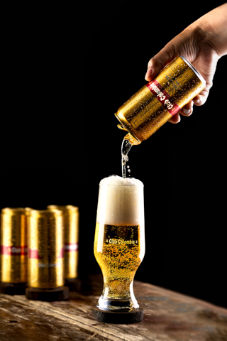 cerveza club Colombia dorada lata, vaso y mano sirviendo